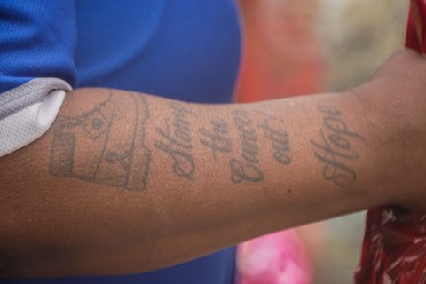 Close-up of a Black woman's arm with a tattoo of the words "Stomp out cancer! Hope" below a shoe.