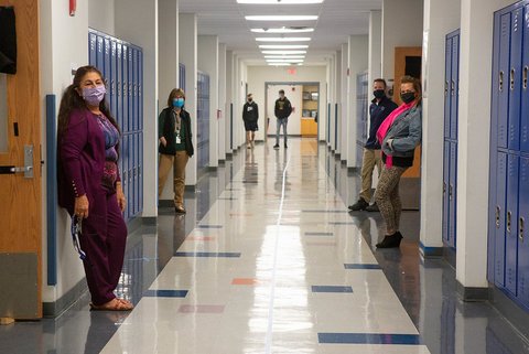 Masked teachers in front of classroom doors in hall lined with lockers