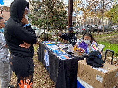 Side view of a Black person looking down at a table covered with fliers staffed by a man and woman