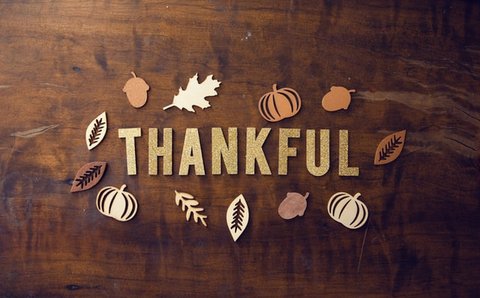 The word "thankful" in gold lettering surrounded by leaf, pumpkin and acorn shapes on a wooden board