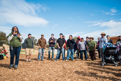 A Black woman with dreadlocks and a microphone and a group of people standing on the site of a new farm