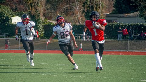 Two high school football players in white and one in red with the ball on the field.