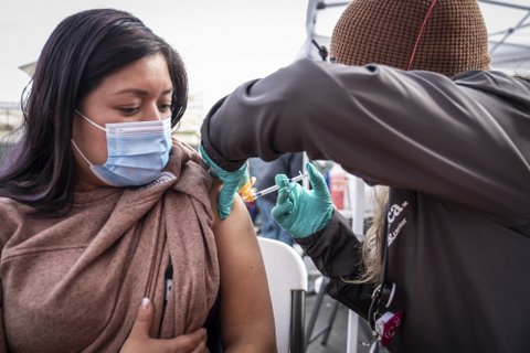 A Latina woman in a medical mask receiving a shot in her upper arm