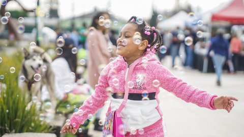 A young Black girl in a pink jacket playing with bubbles
