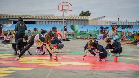 People painting a mural on a basketball court in a park