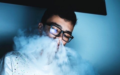 Young man with thick vapor from an e-cigarette coming out of his nose