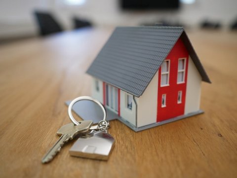 Set of keys on a table next to a figurine of a house with gray roof and red door