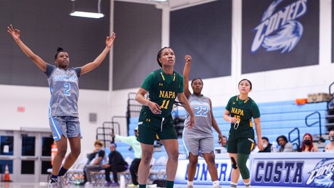 Two women's basketball teammates with one or both arms raised and two opponents on the court