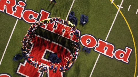 Overhead shot of people standing in a circle on a field with the word "Richmond" in red lettering