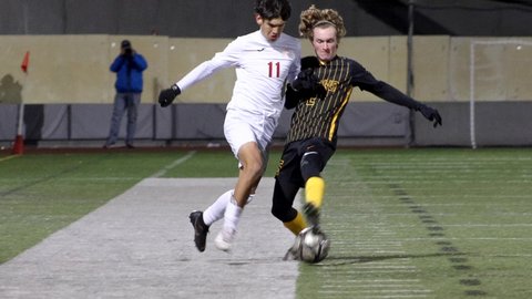 Two opposing soccer players side by side, both going for the ball