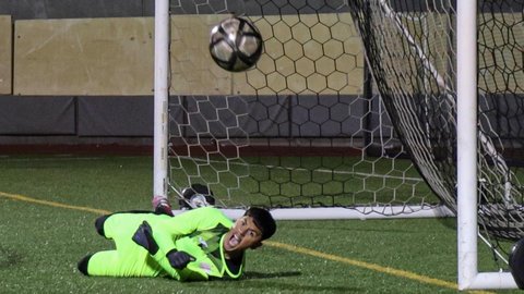 Soccer goalie in neon green yelling with fists balled, on the ground in front of the net with the ball in the air