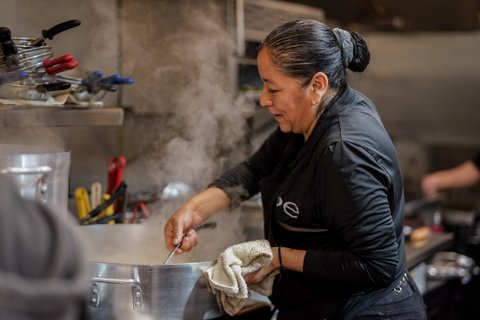 A middle-aged Latina woman dressed in black stirs a pot