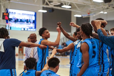 Basketball players bumping fists and raising arms during a timeout.
