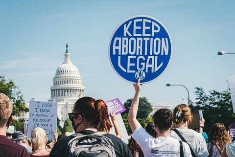 Crowd in which person is holding up sign that says "Keep abortion legal," seen from behind with the Capitol dome visible in the distance