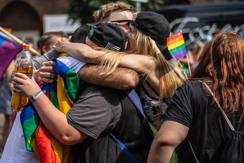Group of young people hugging with rainbow pride flags visible