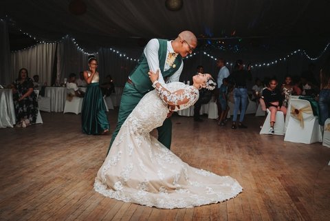 A Black bride and groom on the dance floor. He is dipping her, and they are looking into each other's eyes and smiling.