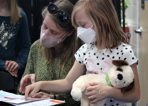 Woman and little girl holding stuffed dog, both wearing masks