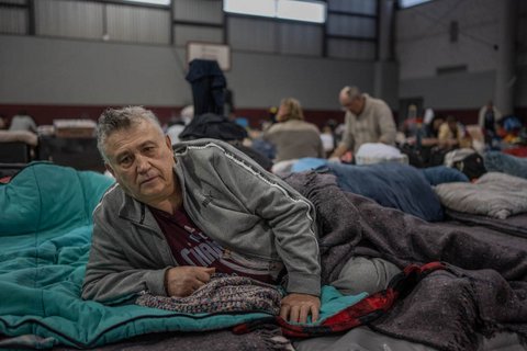 Older man reclining on his side on bed in refugee shelter