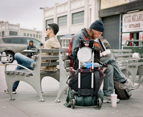 Two men seated on benches, back to back. One is described homeless and the other as wealthy