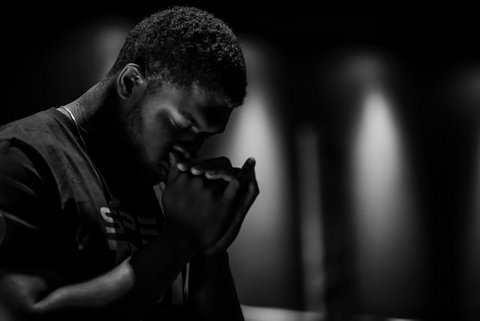 Black-and-white photo of a Black man with his head bowed and hands clasped in prayer
