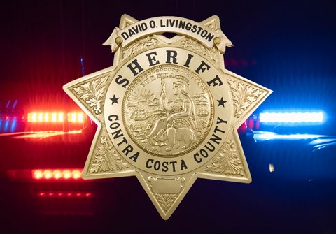 Image of a badge that says David O. Livingston, sherif, Contra Costa County superimposed over image of police lights