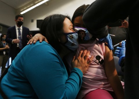 Woman and little girl in masks embracing as girl gets vaccine shot in her arm