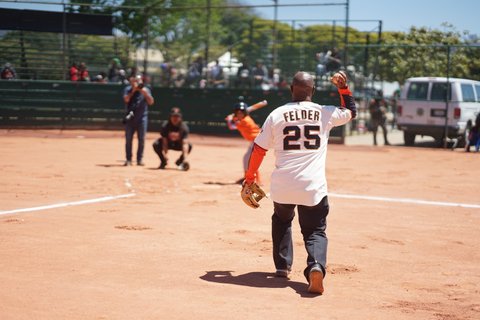 Black man in San Francisco Giants Felder 25 jersey about to throw a pitch on a youth baseball diamond
