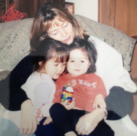 Woman holding her two young daughters in her lap with their heads together