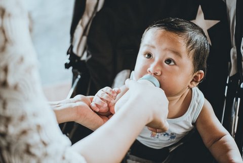 An Asian baby being bottle-fed.