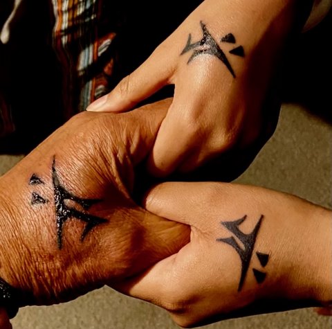 Close ups of the hands of two Black girls holding a Black man's hands. All have matching symbolic tattoos.