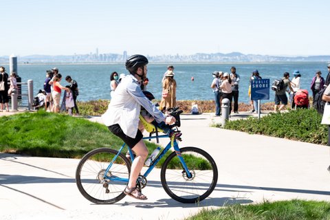 A bicyclist rides by people standing along the shore of the San Francisco Bay