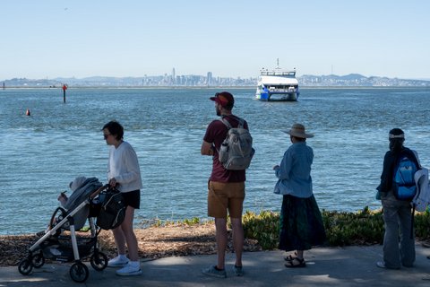People waiting for an approaching ferry with the San Francisco skyline in the background