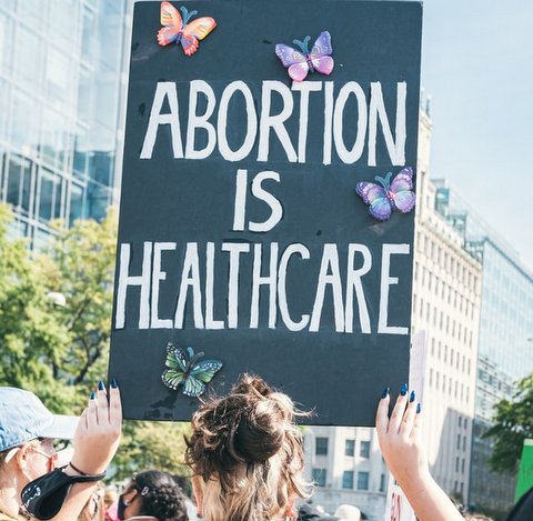 Person seen from behind holding up sign with butterflies on it that says "abortion is healthcare"