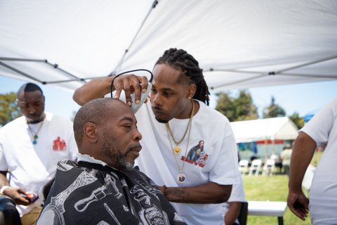 One Black man cuts another Black man's hair with clippers.