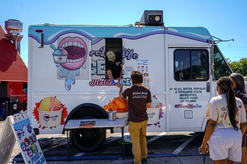 One man hands another a cup of Italian ice from a food truck as two other people look on