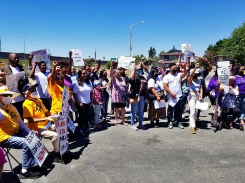 Crowd with signs, some that say "rent control now" or "housing is a human right." People of all ages are in the crowd, including children and seniors