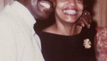 A smiling Black man and woman with his arm around her shoulders and their heads together
