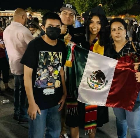Two young men, a young woman and their mother. It is the girl's high school graduation. One of the boys is wearing a mask. A Mexican flag is being held up.