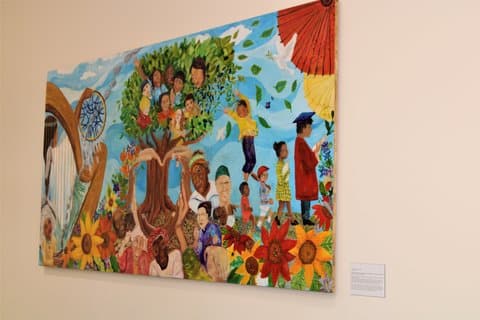 Colorful painting depicting people of different races, some of them in a tree, a harp, dove, blue sky, flowers and leaves blowing in the wind. One child is dressed for a baseball game, another for graduation.