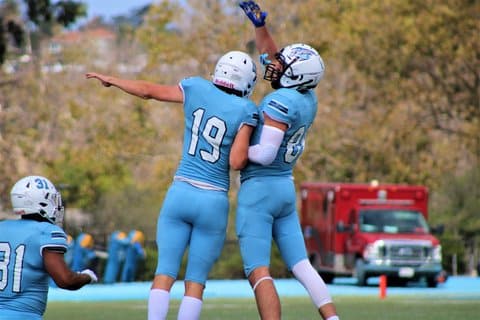 Two football players leaping in the air, each with an arm outstretched, in celebration