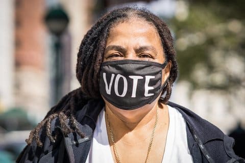 Black woman wearing a face mask with the word vote on it