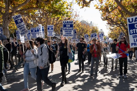 Young adults marching with signs that say UAW on strike unfair labor practice