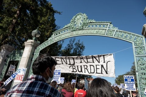 Sather Gate at UC Berkeley with a banner stretched across it that says "end rent burden." There is a crowd. Some people are holding signs that say UAW on strike