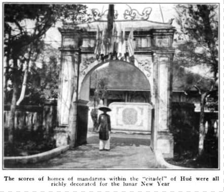 Black-and-white photo captioned "The scores of homes of mandarins within the 'citadel' of Hué were all richly decorated for the lunar New Year." A person in traditional garb is standing in front of a walled enclosure.