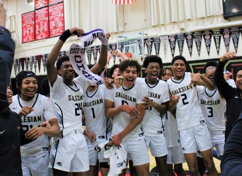 High school boys basketball players celebrating a title win. One is holding up their pennant