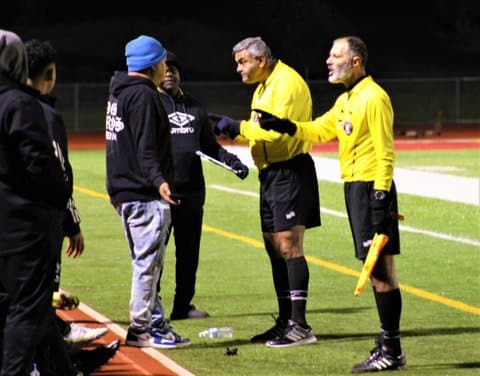 Two soccer referees in yellow communicating with coaches