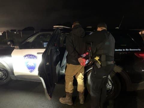 Police officer putting handcuffed man into Antioch Police car.