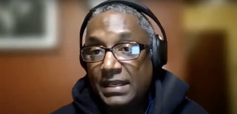 A Black man with graying hair wearing glasses and headphones
