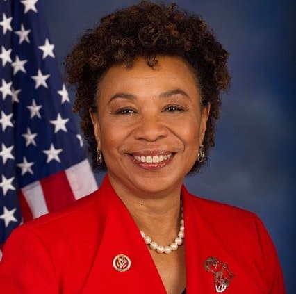 A head-and-shoulders shot of congressional Representative Barbara Lee, a Black woman, in front of a U.S. flag. She is wearing a red jacket with an Africa lapel pin and pearl necklace.