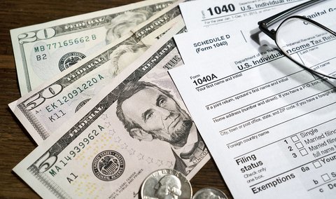 A pile of U.S. tax forms and currency along with a pair of eyeglasses